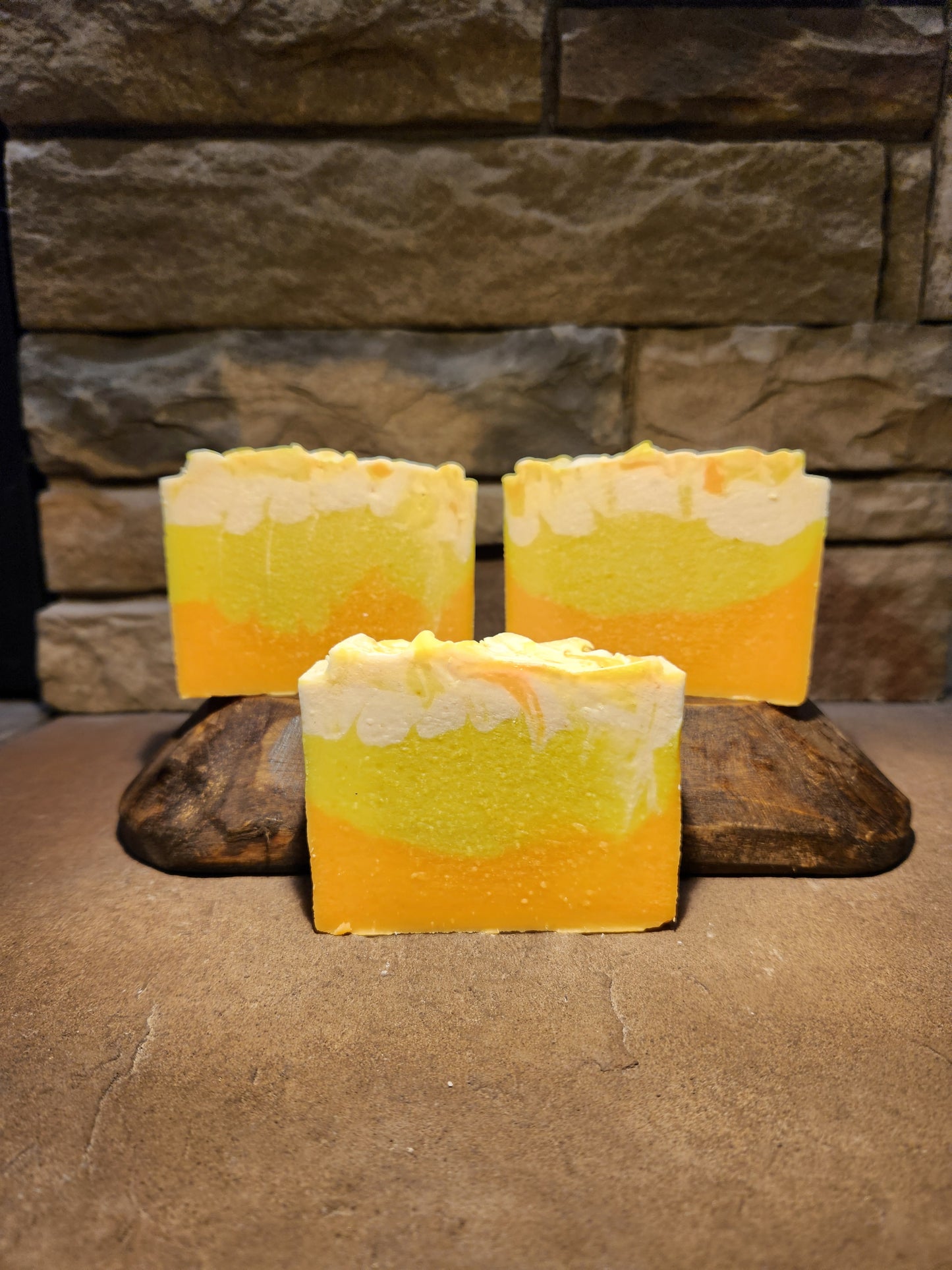 Three orange, yellow and white soap bars sitting on a wood display with a stone background.