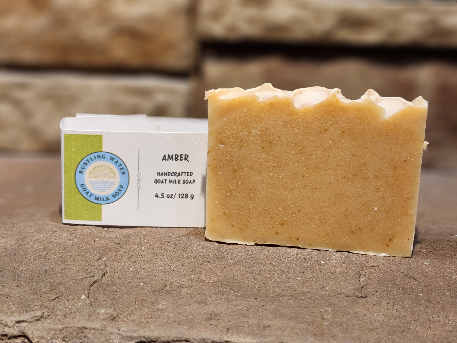 Bar of amber-colored soap next to its packaging on a stone surface
