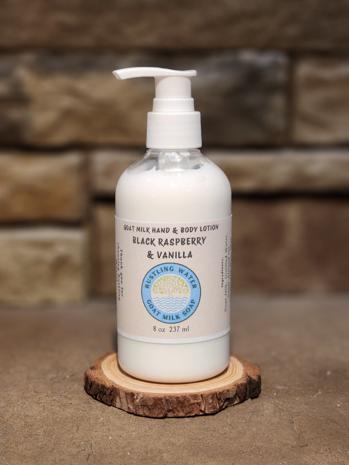 Bottle of goat milk hand and body lotion with a pump on a wooden coaster against a stone wall background.