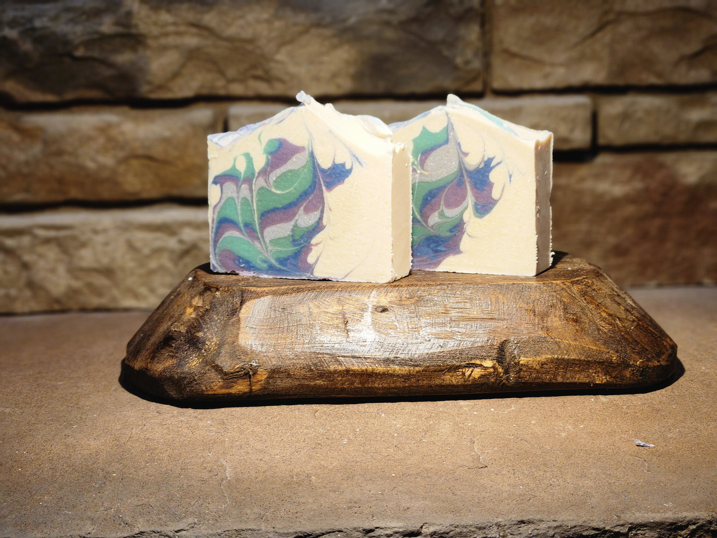 Two multicolored soap bars on a wooden display with a stone background.