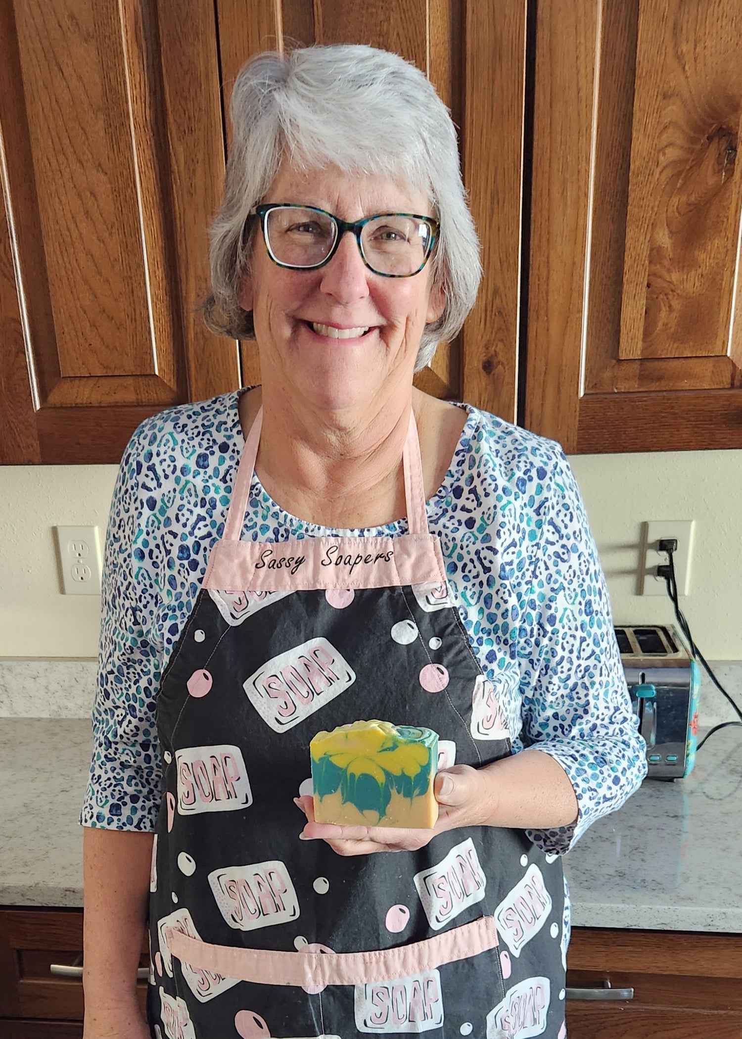 Woman in kitchen wearing an apron holding a tri-colored bar of soap,