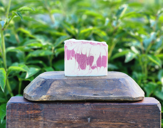 Bar of soap with pink and white design on a wooden block against a green leafy background