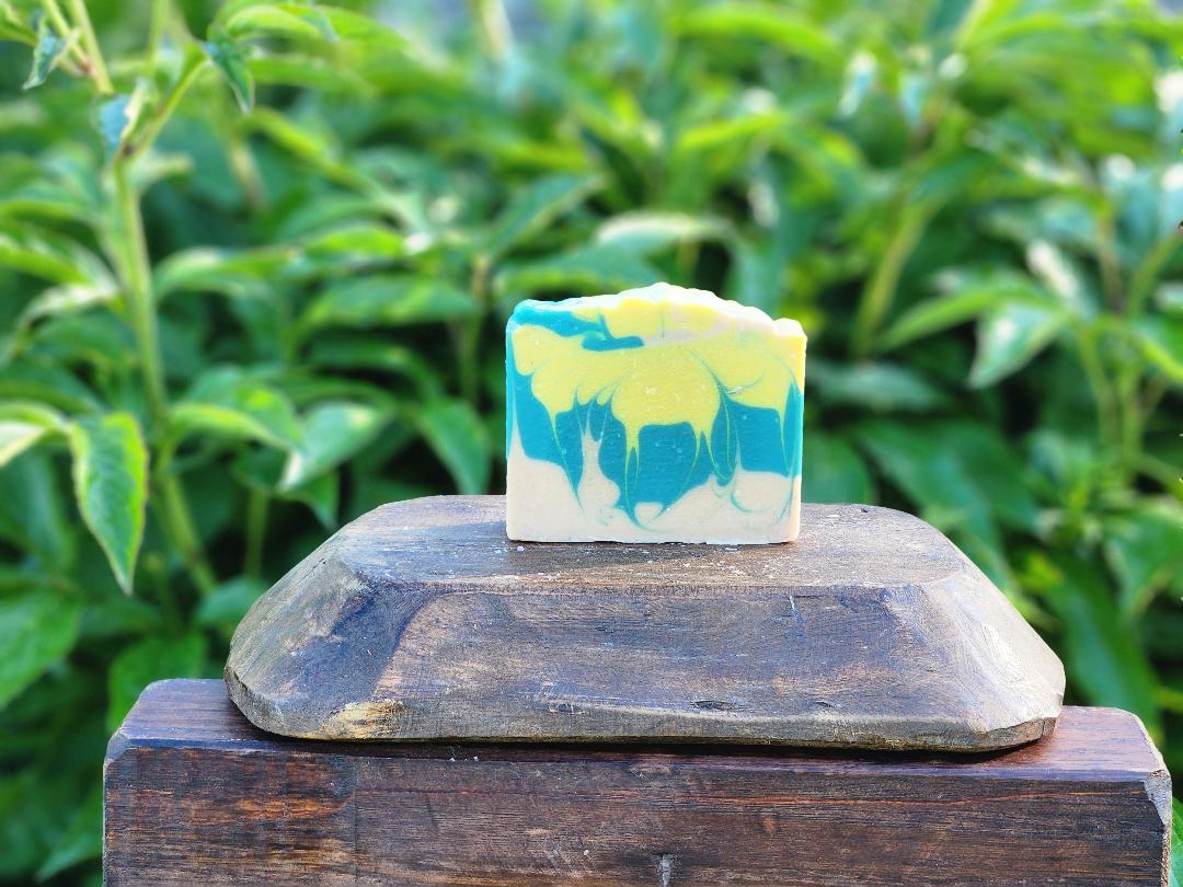 Soap bar with yellow, blue and beige colors on a wooden display with a green leafy background.