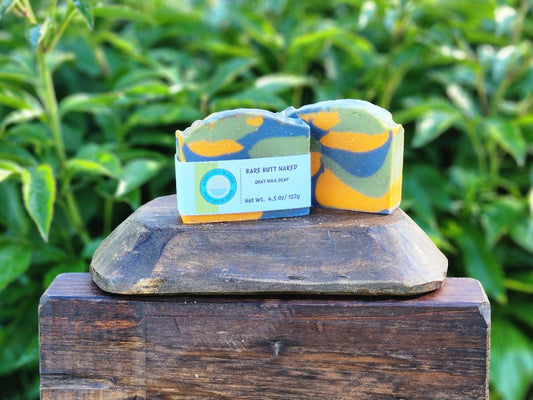 Two bars of soap with a colorful design on a wooden block against a green leafy background
