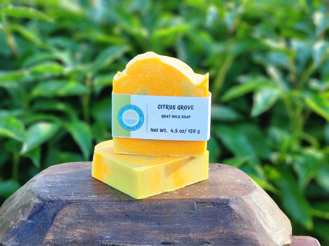 Two yellow soap bars stacked on a wooden block with a green leafy background