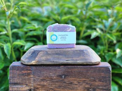 Bar of soap with a label on a wooden block against a green leafy background