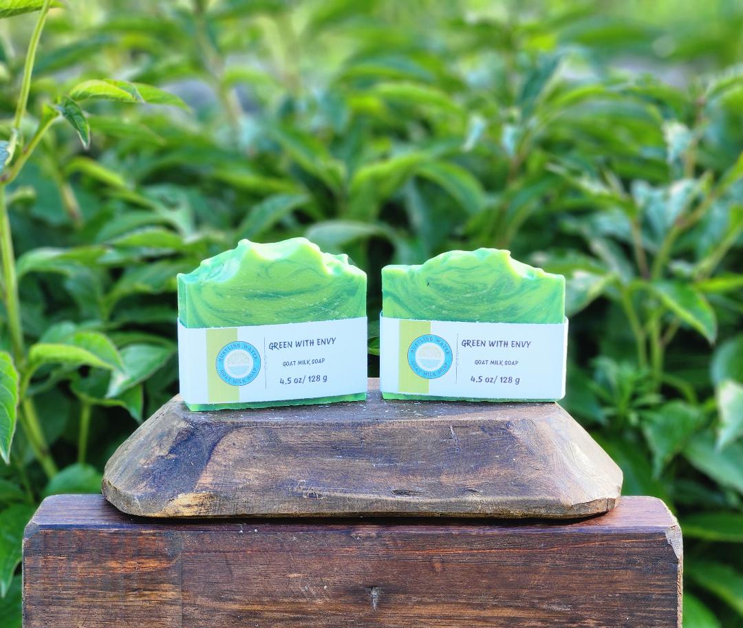 Two green soaps with labels on a wooden block against a natural background