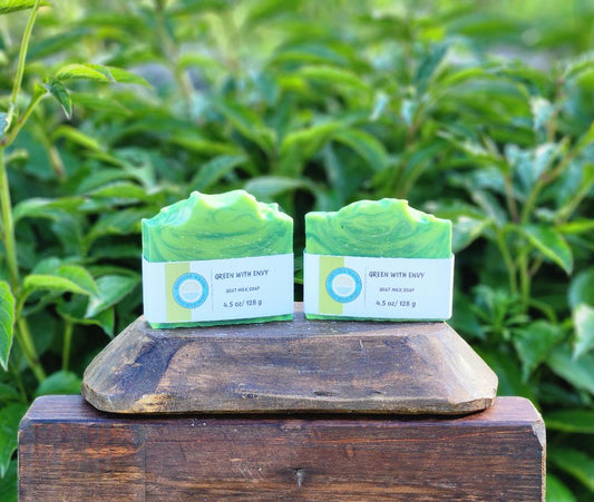 Two green soaps with labels on a wooden block against a natural background