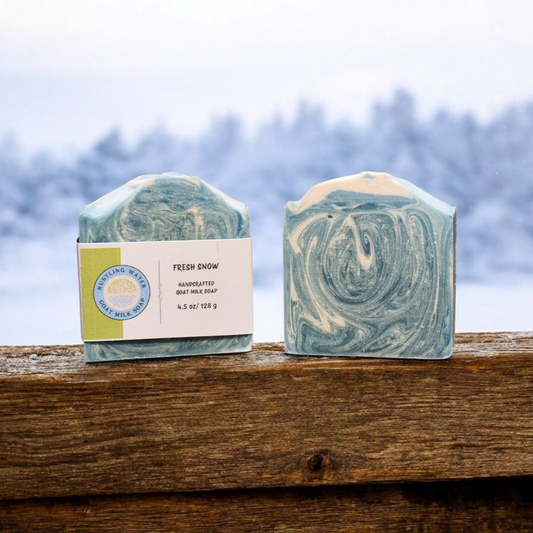 Two swirled soap bars on a wooden surface with a blurred natural background