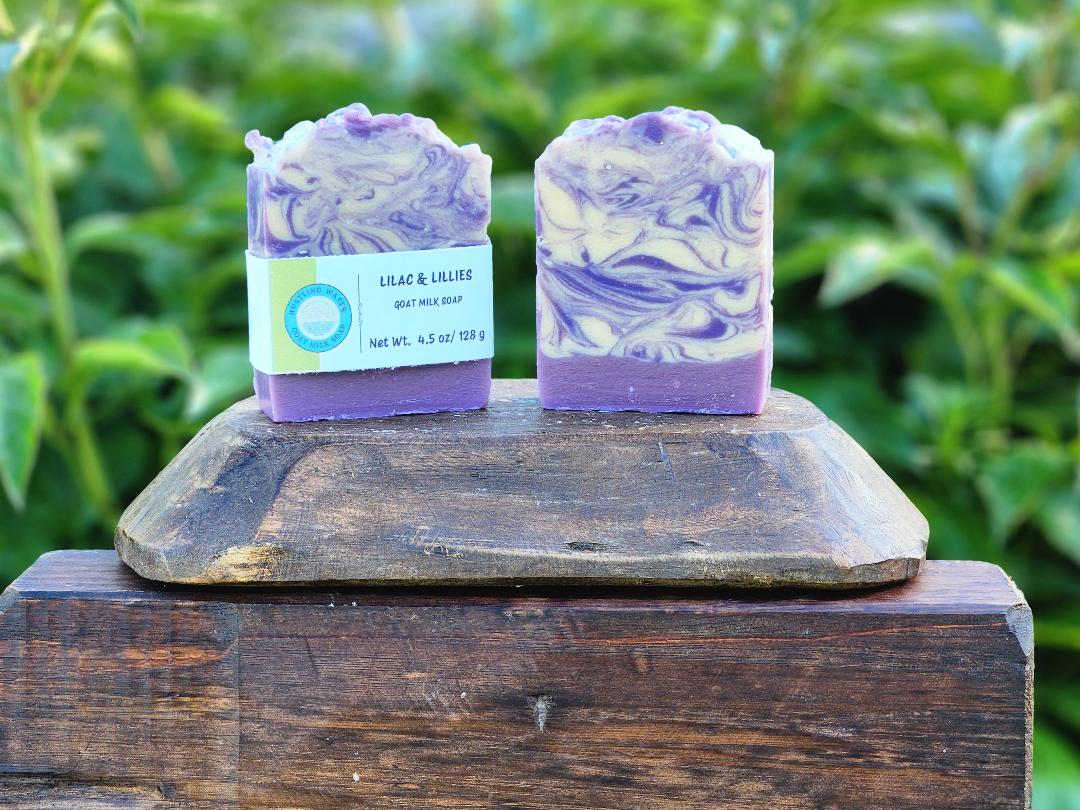 Two bars of purple and white soap on a wooden block with a green leafy background